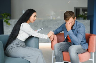 Psychologist talking with patient on therapy session. Depressed man speaking to a therapist while she is taking notes