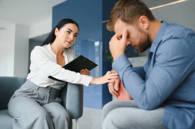Psychologist talking with patient on therapy session. Depressed man speaking to a therapist while she is taking notes