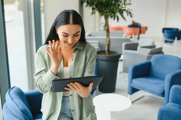 Traveler tourist woman with headphones working on laptop, spreading hands during video call while waiting in lobby hall at airport. Passenger traveling abroad on weekends getaway. Air flight concept.