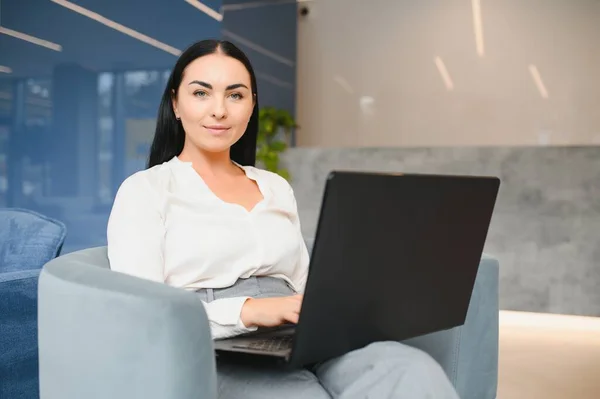 Young business woman sitting at sofa and working with laptop at the waiting hall of the business center.