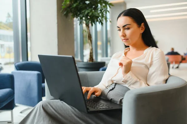 Young business woman sitting at sofa and working with laptop at the waiting hall of the business center.