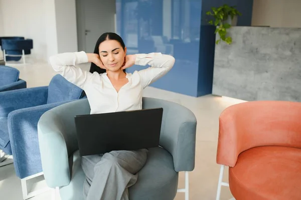 Young business woman sitting at sofa and working with laptop at the waiting hall of the business center.