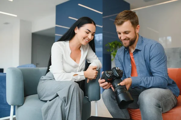 Photographer in office shows photo model in camera. Consultant adjusts activities company as whole. Photo session employees in workplace. Manager well-executed project. Photos best employees company