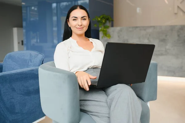 Young business woman sitting at sofa and working with laptop at the waiting hall of the business center.