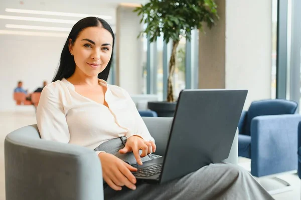 Young business woman sitting at sofa and working with laptop at the waiting hall of the business center.