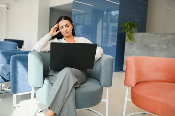 Young business woman sitting at sofa and working with laptop at the waiting hall of the business center.