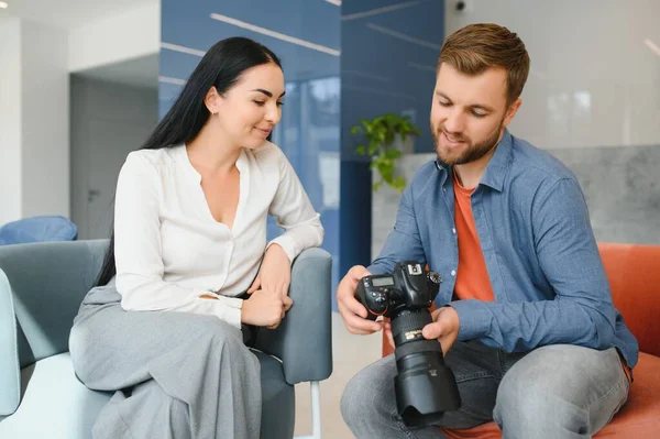 Photographer in office shows photo model in camera. Consultant adjusts activities company as whole. Photo session employees in workplace. Manager well-executed project. Photos best employees company