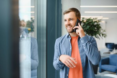 Image of handsome serious young man talking cellphone while working at office