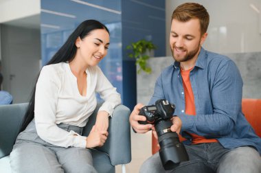 Young photographer man in blue shirt watching photo with client woman after photo session and smiling and looking at each other.