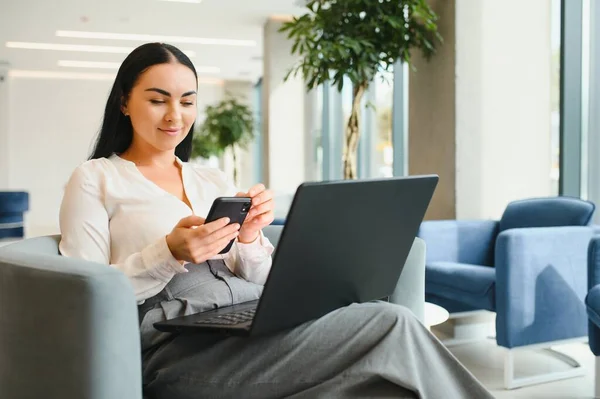 Young business woman sitting at sofa and working with laptop at the waiting hall of the business center.