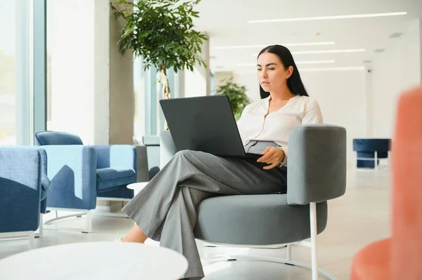 Young business woman sitting at sofa and working with laptop at the waiting hall of the business center.