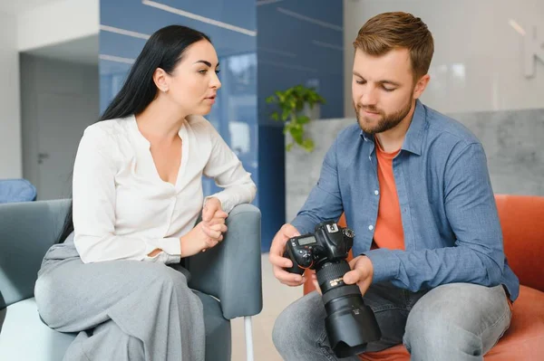 Photographer in office shows photo model in camera. Consultant adjusts activities company as whole. Photo session employees in workplace. Manager well-executed project. Photos best employees company