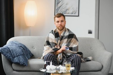 Kötü soğuk algınlığı ya da mevsimsel grip virüsü taşıyan hasta yetişkin bir adam evde hastalıkla savaşıyor. Mutsuz orta yaşlı bir adam sıcak atkı ve ekoseye sarılı olarak koltukta oturuyor, kağıt mendil tutuyor ve hapşırıyor.