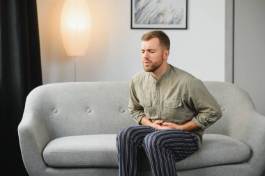 Evde oturma odasında bir kanepede oturan mide ağrısı acı Adam