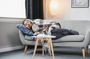 Hasta bir adam gri bir kanepede battaniyeyle oturuyor. Hastalık, koruma, koronavirüs, hastalık, grip..