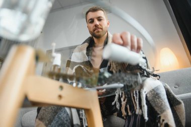 Hasta bir adam gri bir kanepede battaniyeyle oturuyor. Hastalık, koruma, koronavirüs, hastalık, grip..