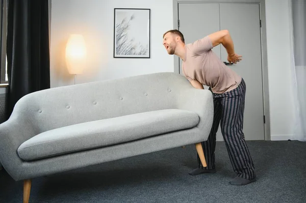 Young man suffering from back pain after carrying heavy furniture