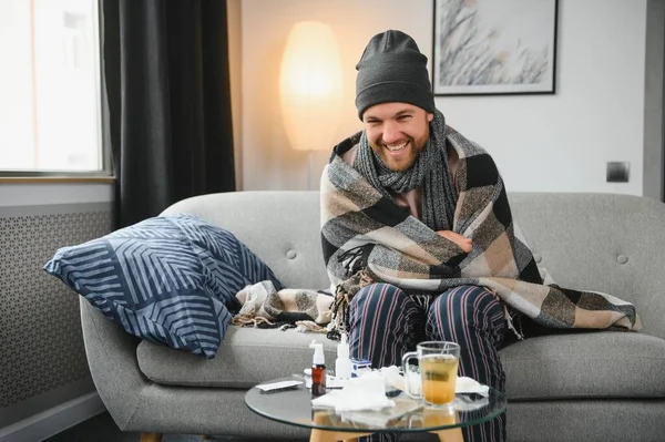 冬は家が寒い 冬はサーモスタットの故障で家で凍える男 リビングルームのインテリアでソファに座っている間にウールのプレイ震えに包まれた若い男 — ストック写真