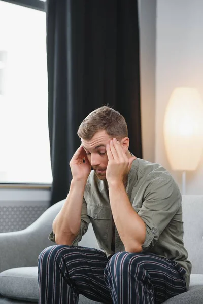 Ill man sitting on his bed with his head on his hand.