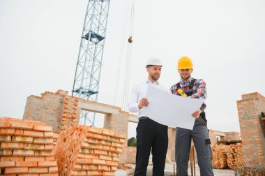 İnşaat mühendisleri inşaat projesinin ilerlemesini denetliyor. Yeni beton zemin üstü çatı ve vinç arka planı üzerinde duruyorlar.