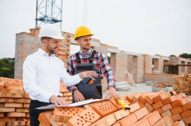 İnşaat mühendisleri inşaat projesinin ilerlemesini denetliyor. Yeni beton zemin üstü çatı ve vinç arka planı üzerinde duruyorlar.