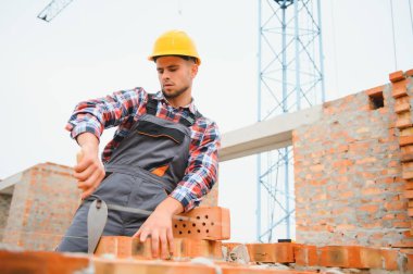 Busy with brick wall. Construction worker in uniform and safety equipment have job on building