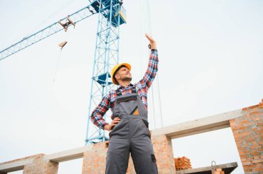 Communicating with crane guy. Construction worker in uniform and safety equipment have job on building