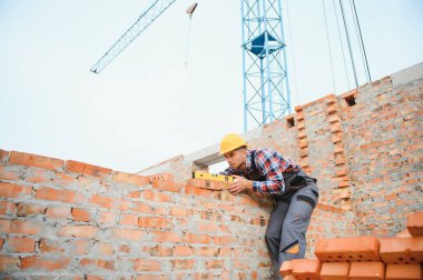 Sarı renkli başlık. Gündüz vakti inşaatta üniformalı genç bir adam çalışıyor.