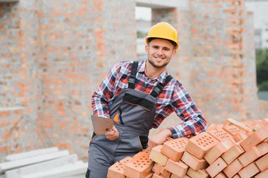 Construction worker man in work clothes and a construction helmet. Portrait of positive male builder in hardhat working at construction site