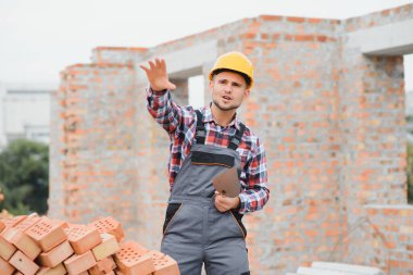 Construction worker man in work clothes and a construction helmet. Portrait of positive male builder in hardhat working at construction site