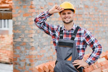 Sarı renkli başlık. Gündüz vakti inşaatta üniformalı genç bir adam çalışıyor.