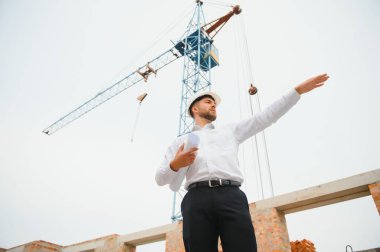 İnşaat mühendisi inşaat projesinin ilerlemesini denetliyor. Yeni beton çatı ve vinç zemin üzerinde duruyor.