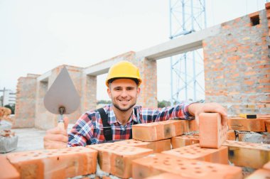 Tuğla duvarla meşgul. Üniformalı inşaat işçisi ve güvenlik ekipmanı inşaatında çalışıyor