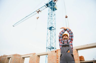 Sarı renkli başlık. Gündüz vakti inşaatta üniformalı genç bir adam çalışıyor.