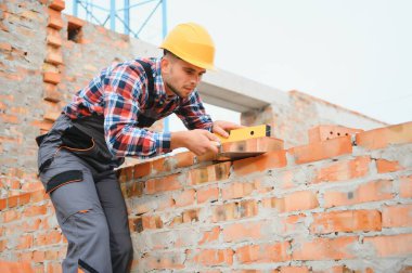 Tuğla duvar kuruluyor. Üniformalı inşaat işçisi ve güvenlik ekipmanı inşaatında çalışıyor.