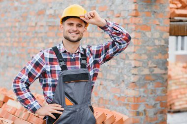 Construction worker man in work clothes and a construction helmet. Portrait of positive male builder in hardhat working at construction site