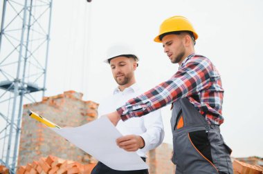 İnşaat mühendisleri inşaat projesinin ilerlemesini denetliyor. Yeni beton zemin üstü çatı ve vinç arka planı üzerinde duruyorlar.