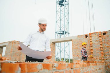 İnşaat alanındaki Mühendislik Danışmanlığı elinde planları tutuyor. İnşaat müfettişi. Yeni binanın inşaat sahası çizimi ve iş akışı