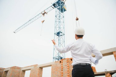 İnşaat mühendisi inşaat projesinin ilerlemesini denetliyor. Yeni beton çatı ve vinç zemin üzerinde duruyor.