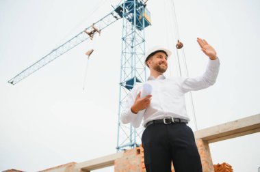 İnşaat mühendisi inşaat projesinin ilerlemesini denetliyor. Yeni beton çatı ve vinç zemin üzerinde duruyor.