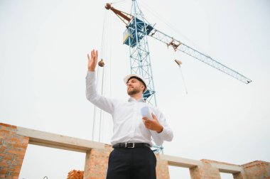 İnşaat mühendisi inşaat projesinin ilerlemesini denetliyor. Yeni beton çatı ve vinç zemin üzerinde duruyor.