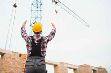 Vinçli adamla iletişim kuruyorum. Üniformalı inşaat işçisi ve güvenlik ekipmanı inşaatında çalışıyor