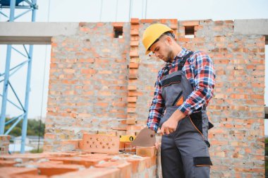 Sarı renkli başlık. Gündüz vakti inşaatta üniformalı genç bir adam çalışıyor.