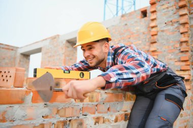 Sarı renkli başlık. Gündüz vakti inşaatta üniformalı genç bir adam çalışıyor.