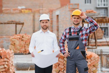 Başlık ve güvenlik yeleği giyen mühendis büyük inşaat alanında takım halinde çalışıyor..