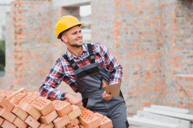Sarı renkli başlık. Gündüz vakti inşaatta üniformalı genç bir adam çalışıyor.