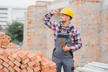 Construction worker man in work clothes and a construction helmet. Portrait of positive male builder in hardhat working at construction site