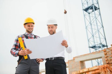 İnşaat alanının planlarını tartışan sert şapkalı mühendis ve müteahhit