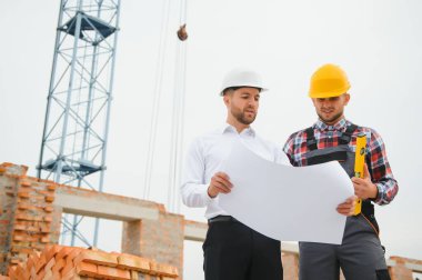 İnşaat mühendisleri inşaat projesinin ilerlemesini denetliyor. Yeni beton zemin üstü çatı ve vinç arka planı üzerinde duruyorlar.