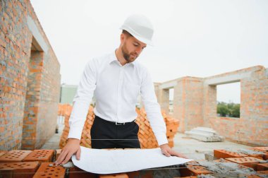 İnşaat alanındaki Mühendislik Danışmanlığı elinde planları tutuyor. İnşaat müfettişi. Yeni binanın inşaat sahası çizimi ve iş akışı